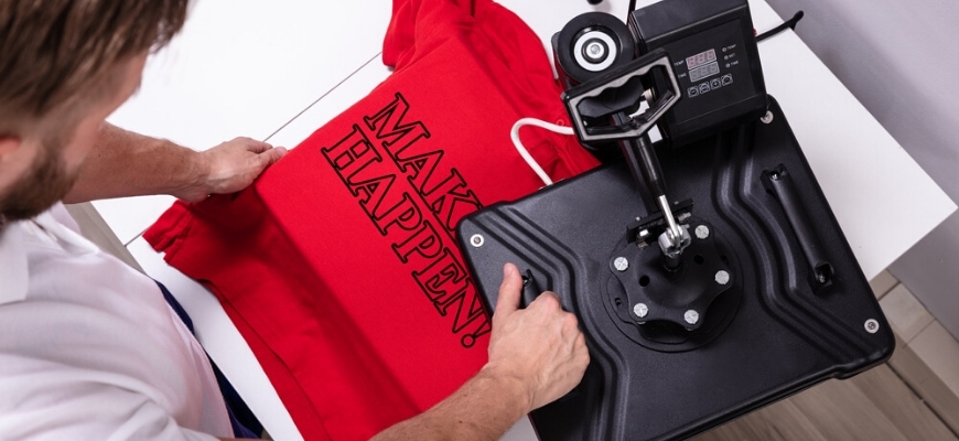 Cropped top view of man painting red shirt using a heat press.