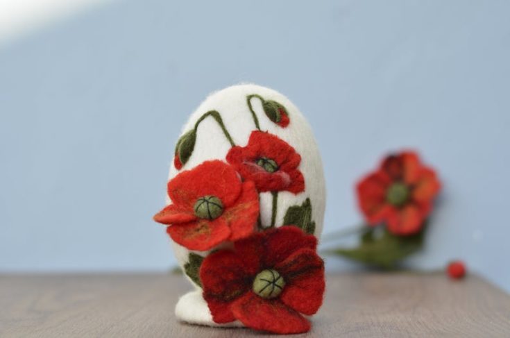 A felt easter egg craft design with red flowers on top of the table.