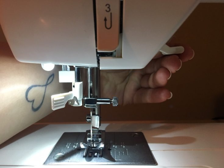 a person's hand holding the Thread take-up lever of the sewing machine