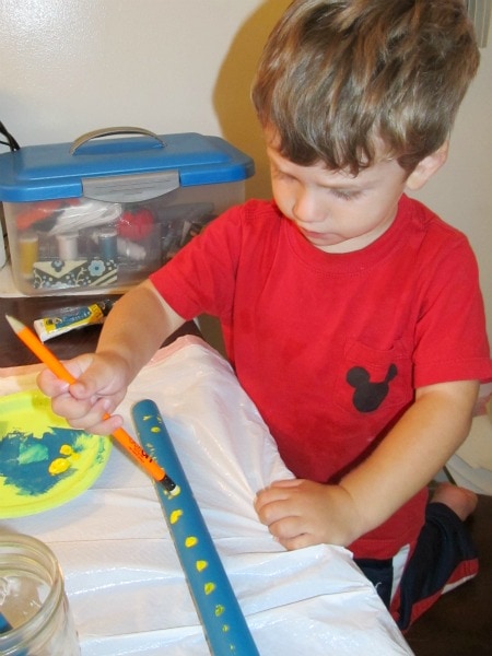 a boy in red shirt painting the blue wooden dowel