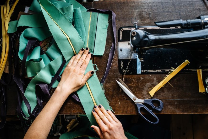 Womann's hand holding cloth on the table of sewing machine with scissor on the side