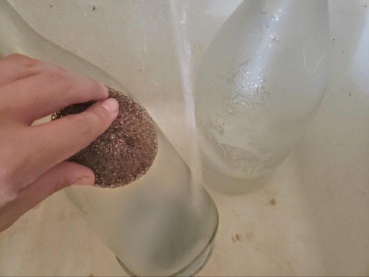 Close up shot of hand holding a scrubber to remove label on wine battle.