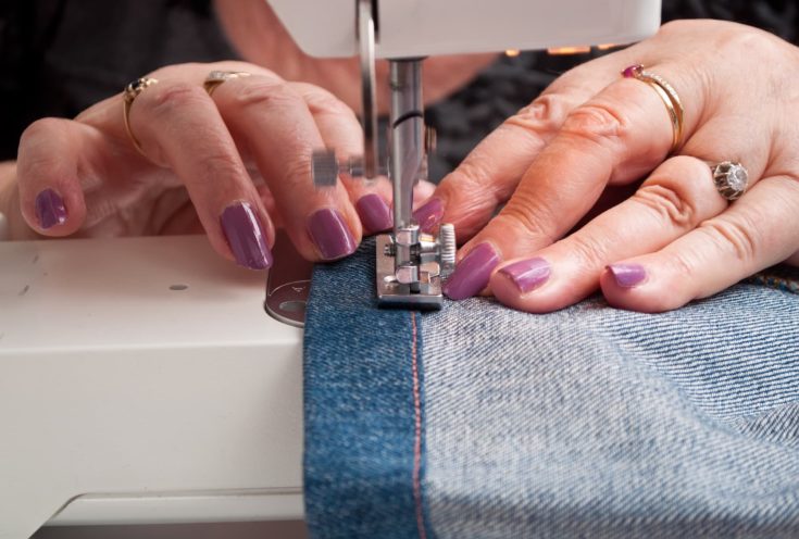 closeup of woman with a sewing machine and blue jeans hem