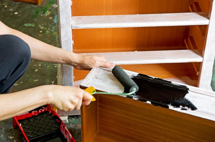 painter with paint roller painting a wooden commode