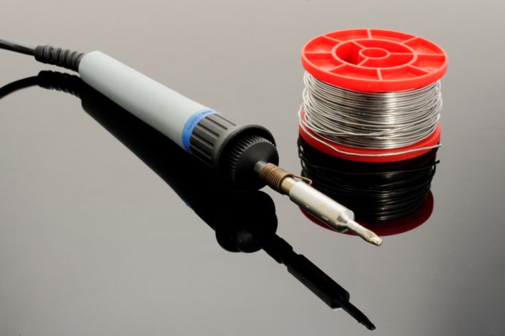 Closeup view soldering iron laid on wooden table.
